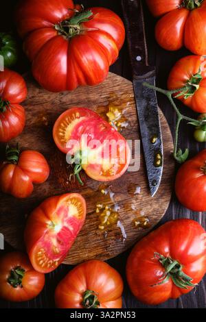 Ein Schuss frischer roter Tomaten auf einem runden Holzbrett mit einem alten Messer auf einem rustikalen Tisch Stockfoto