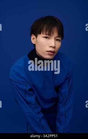 Ein selbstbewusster junger Mann zeigt moderne Mode und verströmt Charme mit einem auffälligen blauen Hintergrund. Stockfoto