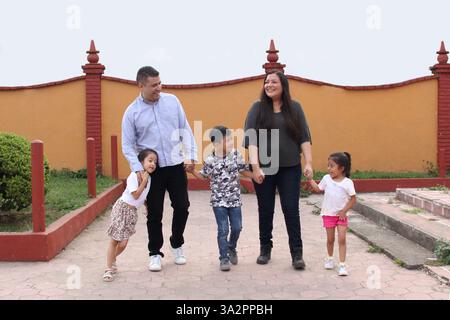 Brünette Latin Familie von Vater, Mutter, Töchtern und Sohn spazieren zusammen im Park Hand in Hand verbringen schöne Zeit Stockfoto