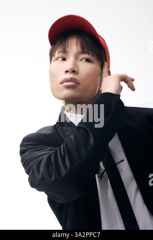 Der hübsche junge Mann steht vor einem schlichten Hintergrund und zeigt trendigen Stil und Charisma. Stockfoto