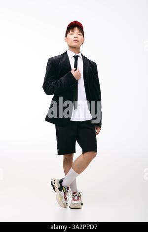 Ein selbstbewusster junger Mann, der eine stylische schwarze Anzugsjacke über Shorts trägt, posiert im Studio. Stockfoto