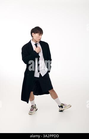 Ein hübscher junger asiatischer Mann zeigt ein modernes Modeensemble mit Shorts und langem Mantel. Stockfoto