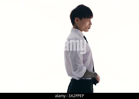 Scharf gekleideter junger Mann mit Tätowierungen, die Charisma und Eleganz vor einem minimalen Hintergrund ausstrahlen. Stockfoto