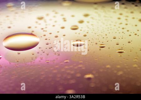 Makrodetails von Wassertropfen auf einer metallischen Oberfläche mit Gold- und Rosa-Farben, die Luxus und Eleganz anzeigen, perfekt für Hintergründe. Stockfoto