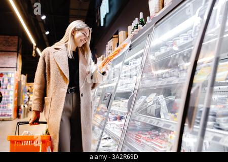 Junge Frau, die Lebensmittel kauft, verpackte Lebensmittel aus dem Kühlbereich im Supermarkt sammelt Stockfoto