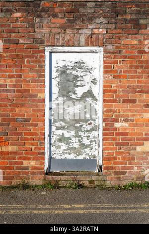 Alte Tür mit abblätternder weißer Farbe und einer roten Ziegelwand Stockfoto