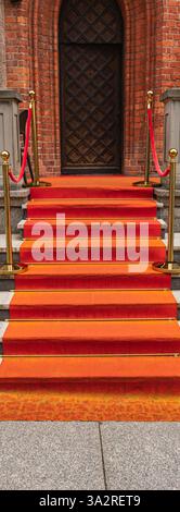 Roter Teppich auf den Stufen vor der alten Holztür zum Gebäude Stockfoto