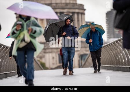 Menschen, die Regenschirme tragen, laufen durch den Regen auf der Millennium Bridge in London, nachdem Teile Englands in den frühen Morgenstunden von starkem Regen und Überschwemmungen heimgesucht wurden. Bilddatum: Freitag, 27. September 2024. Stockfoto