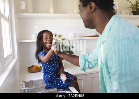 Afroamerikanischer Vater und Tochter genießen spielerische Momente beim Händewaschen in der Küche Stockfoto