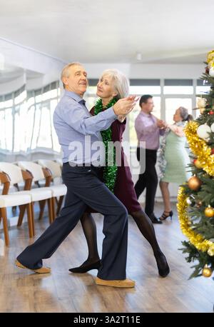 Aktive ältere Menschen feiern Weihnachten und tanzen Tango im Ballsaal Stockfoto
