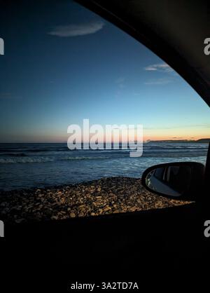 Abendlicher Blick auf Kourion Beach in Zypern, von einem geparkten Auto aus aufgenommen, während das letzte Licht über dem Meer verblasst. Stockfoto