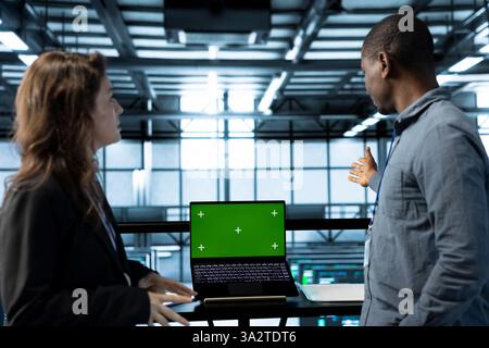 Team von Serverfarmen, die einen Laptop mit isoliertem Bildschirm verwenden, Sicherheitsaudits durchführen und Fehler vermeiden. IT-Experten im Rechenzentrum überprüfen Firewall-Regeln auf Chroma Key-Geräten Stockfoto