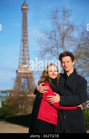Ein glückliches Paar umarmt sich an einem sonnigen Tag vor dem Eiffelturm und genießt einen romantischen Moment zusammen in Paris. Stockfoto