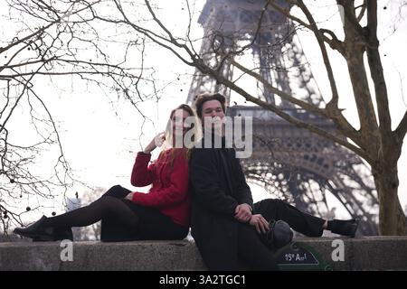 Ein modisches junges Paar lehnt sich auf einem Steinvorsprung nahe dem Eiffelturm gegeneinander, um eine entspannte Pariser Atmosphäre zu genießen. Stockfoto