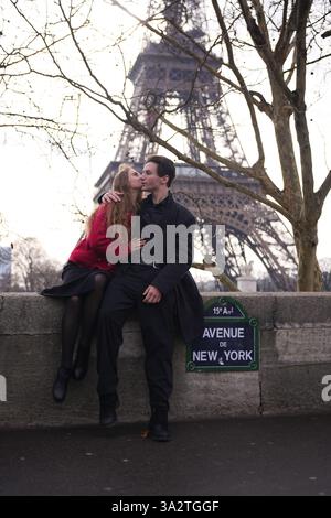 Ein junges Paar genießt einen romantischen Moment auf der Avenue de New York in Paris, hinter dem sich der Eiffelturm erhebt. Die Frau lehnt sich zu einem Kuss hin und hält eine intime und stilvolle Szene fest. Stockfoto