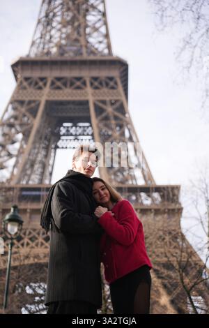 Ein liebevolles Paar umarmt sich in der Nähe des Eiffelturms in Paris. Die Frau lehnt sich auf die Brust des Mannes und schafft einen zärtlichen und liebevollen Moment. Stockfoto