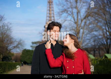 Ein fröhliches Paar umarmt sich vor dem Eiffelturm und teilt einen romantischen und liebevollen Moment im malerischen Pariser Park. Stockfoto