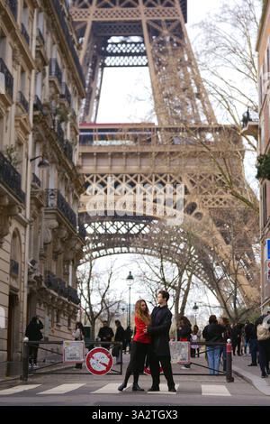 Paris, Frankreich 03.10.2025 Ein stilvolles Paar umarmt in einer malerischen Pariser Straße mit dem Eiffelturm im Hintergrund, umgeben von Stadtleben und Architektur. Stockfoto