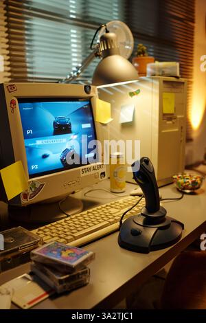 Retro-Spielstation mit klassischem Computer mit Monitor, Joystick und Tastatur. Vintage-Gaming-Erinnerungsstücke werden um den Schreibtisch gelegt und geben so eine nostalgische Atmosphäre Stockfoto