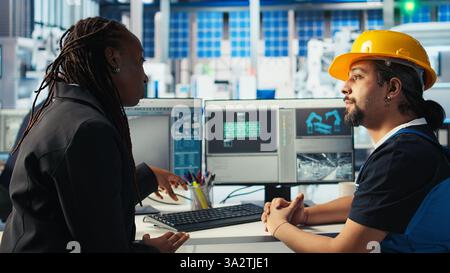Arbeiter in der Photovoltaik-Fabrik diskutiert mit Frau über die Systemleistung. Produktionsanlage für Solarpaneele afroamerikanischer Manager im Gespräch mit Ingenieur über Energieerzeugung, Kamera A Stockfoto