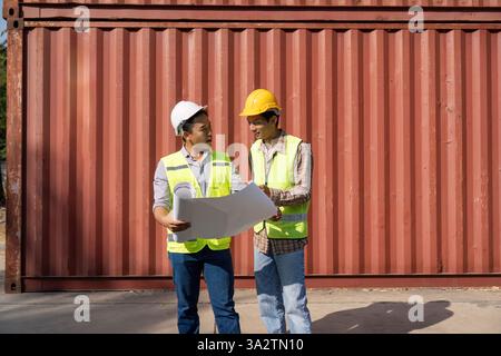Kollaborative Konstruktion. Zwei Ingenieure diskutieren Logistikpläne vor Versandcontainern. Stockfoto