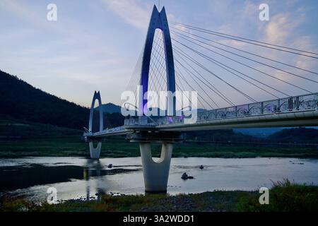 Gurye County, Südkorea - 3. Oktober 2021: Die Krötenbrücke leuchtet in der Dämmerung mit sanftem violettem Licht und überspannt den Seomjin River. Das moderne Fahrerhaus Stockfoto