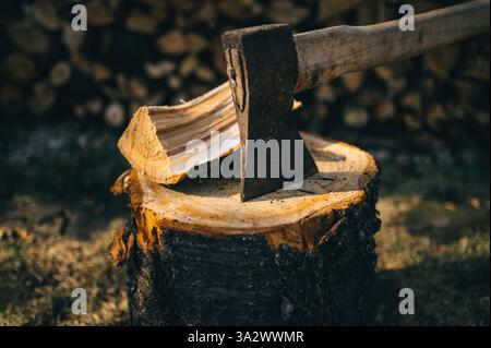 Alte Axt steckt in einem Holzblock auf dem Hintergrund von Brennholz Stockfoto