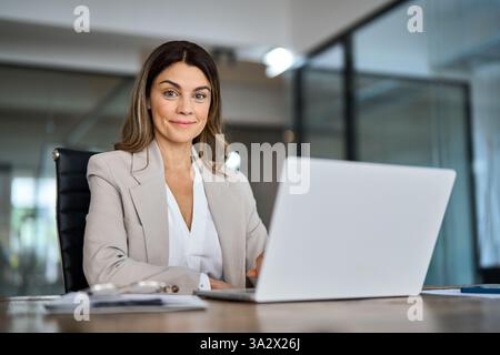 Lächelnde Geschäftsfrau mittleren Alters, die im Büro am Laptop arbeitet, Porträt. Stockfoto