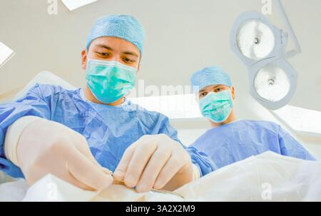 Chirurgen in chirurgischer Kleidung und Maske operieren unter sterilen Bedingungen in einem modernen Operationssaal. Das Bild zeigt einen Fokus auf Teamwork und Stockfoto