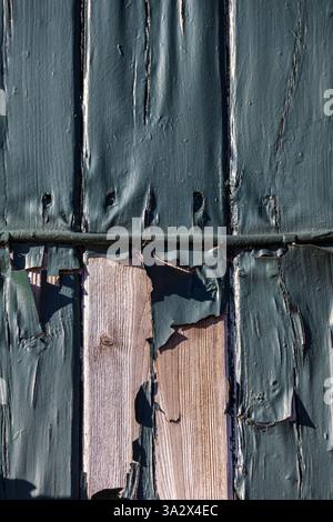 Grüne Farbe, die von einer Holzdielen-Fassade abblättert, über die ein elektrisches Kabel verläuft, ebenfalls mit derselben verwitterten Schicht beschichtet, was das Alter deutlich macht Stockfoto