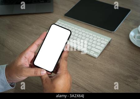 Ein kluger Mensch benutzt einen Laptop und ein Smartphone an einem modernen Schreibtisch, hält ein Telefon in einer Hand und tippt auf einer Tastatur, um digitale Kommunikation anzuzeigen Stockfoto