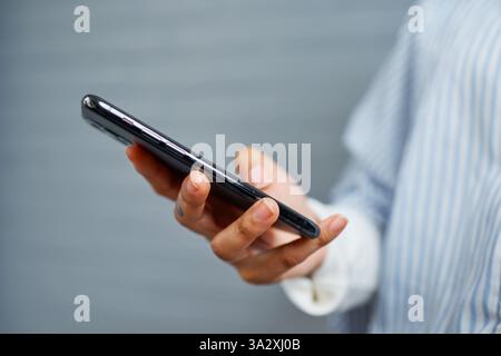 Person, die das Smartphone in der Hand hält, während sie im legeren Outfit steht Stockfoto