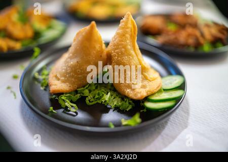 Eine köstliche Auswahl an indischer Küche auf einer unberührten weißen Tischdecke mit Samosas, Pakoras, Curry und Beilagen aus frischen Gurken und Stockfoto