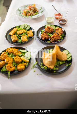 Eine köstliche Auswahl an indischer Küche auf einer unberührten weißen Tischdecke mit Samosas, Pakoras, Curry und Beilagen aus frischen Gurken und Stockfoto