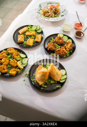 Eine köstliche Auswahl an indischer Küche auf einer unberührten weißen Tischdecke mit Samosas, Pakoras, Curry und Beilagen aus frischen Gurken und Stockfoto