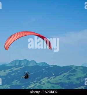 Tandem-Gleitschirmflug auf der Schmittenhöhe in Zell am See, Österreich mit leuchtendem, solidem roten Flügel. Stockfoto