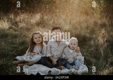 Wunderschönes Porträt von drei Geschwistern, die draußen auf Messingfeld sitzen Stockfoto