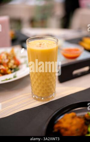 Erfrischende Mango-Lassi serviert in eleganten Gläsern auf dem Tisch mit indischen Vorspeisen und Saucen, die die lebendige kulinarische Kultur von verkörpern Stockfoto