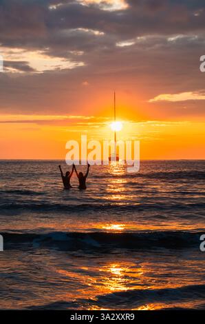 Paare mit Händen in der Luft, die den wunderschönen Sonnenuntergang im Meer beobachten. Stockfoto