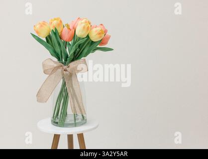 Eine Vase gefüllt mit gelben und rosa Tulpen, gebunden mit einem Sackleinen bo Stockfoto