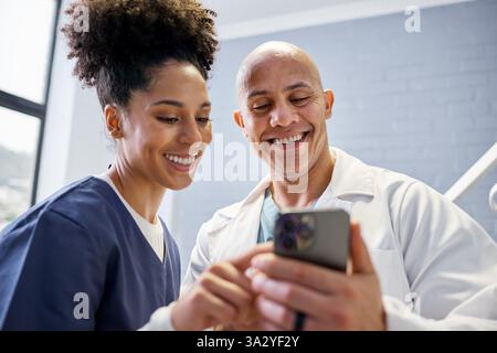 Zwei medizinische Fachkräfte lächeln und teilen Informationen auf einem Smartphone Stockfoto