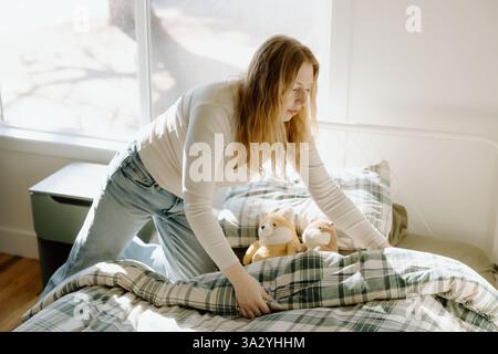 Eine Mutter macht das Bett in einem hellen, gemütlichen Schlafzimmer Stockfoto