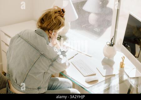 Eine Geschäftsfrau konzentriert sich während ihrer Arbeit an ihrem hellen Schreibtisch im Home Office. Stockfoto