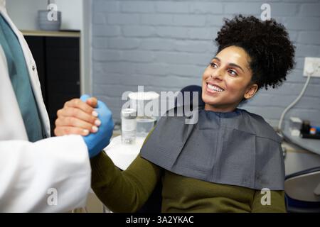 Lächelnder Patient in der Pflege während eines Zahnarzttermins und Händeschütteln beim Zahnarzt Stockfoto