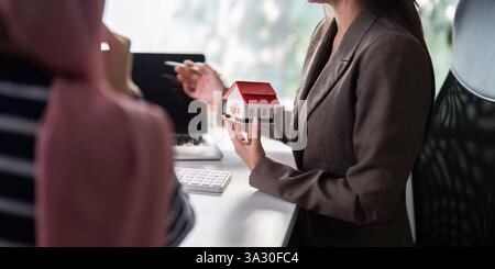 Immobilienpräsentation und Hauskauf. Ein Immobilienmakler erläutert während eines Meetings die wichtigsten Merkmale einer Immobilie anhand eines Musterhauses. Stockfoto