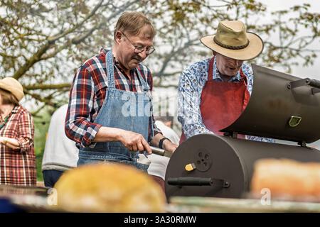 Zwei ältere Männer kochen gemeinsam auf einem Grill auf einer Gartenparty im Freien, genießen Teamarbeit, Freundschaft und aktiven Lebensstil. Außenkochfeld Stockfoto