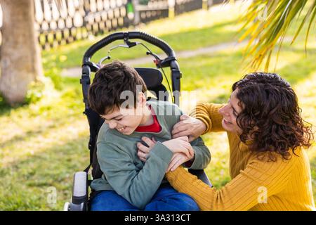 Glückliche Mutter, die mit einem behinderten Sohn im Rollstuhl im Freien spielt Stockfoto