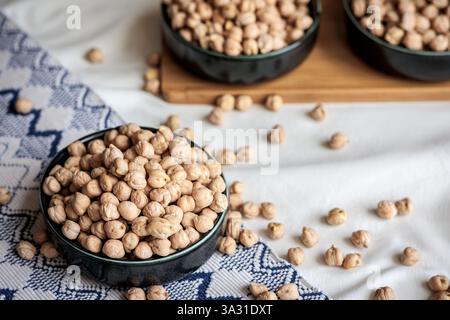 Eine Komposition aus getrockneten Kichererbsen in Keramikschalen auf einem weichen Stoff und Holztablett, die natürliche Texturen und gesunde Ernährung in einem minimalistischen s hervorheben Stockfoto