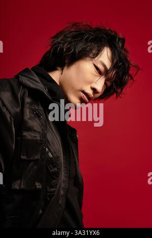 Ein junger asiatischer Mann posiert in einem Studio. Er trägt ein stilvolles, dunkles Ensemble. Stockfoto