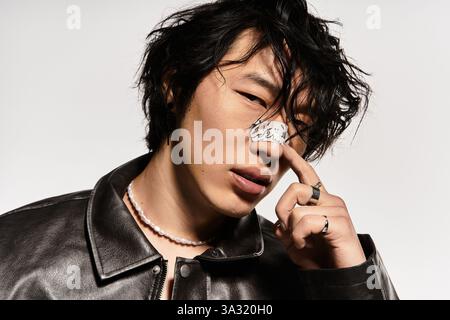 Ein junger asiatischer Mann in Lederjacke und Gips auf der Nase posiert in einem Studio. Stockfoto